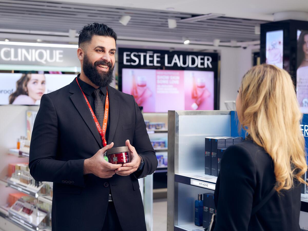 A smiling man showing a cream to a female customer.