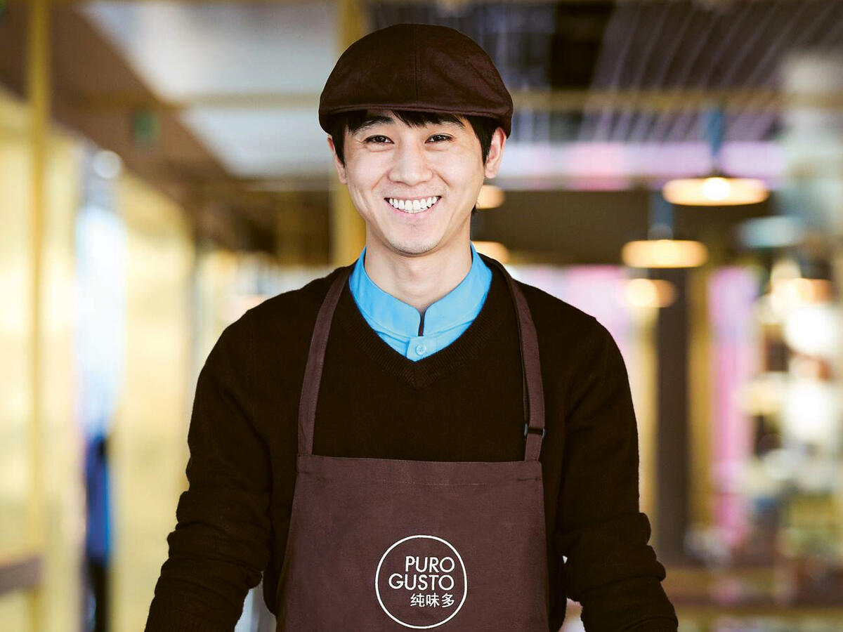 A smiling asian male employee wearing a Puro Gusto's apron.