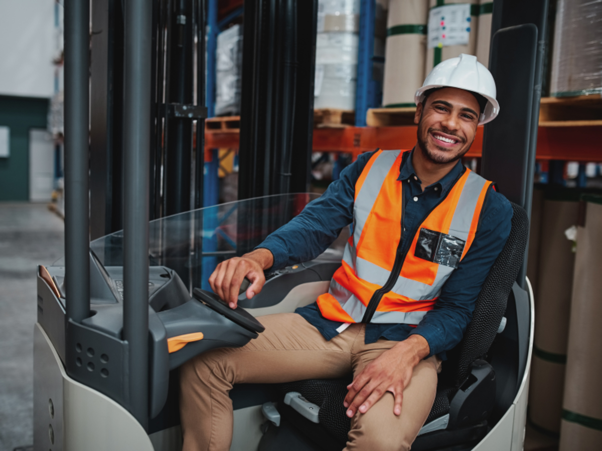A guy wearing a safety helmet on a forklift.
