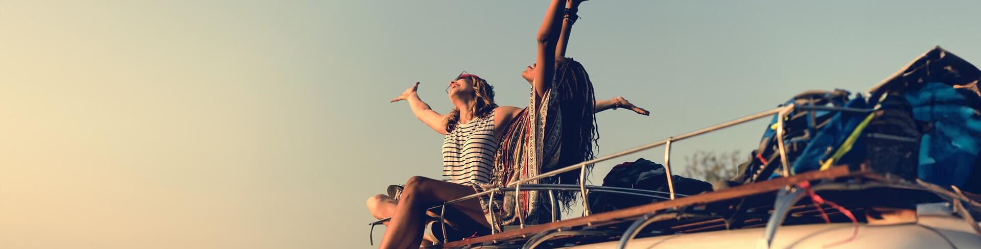 Travelers sat on a camper van with arms in the air
