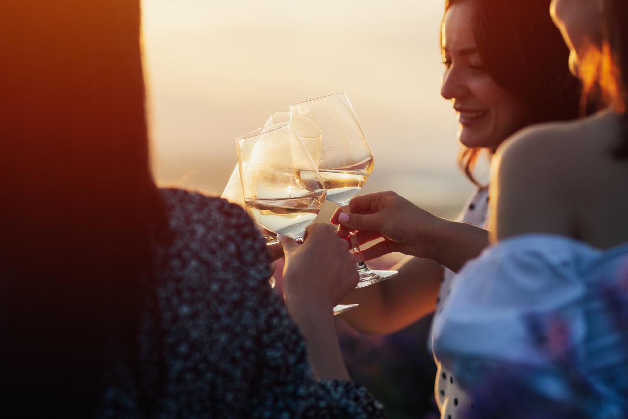 Two people toasting with white wine against a sunset backdrop