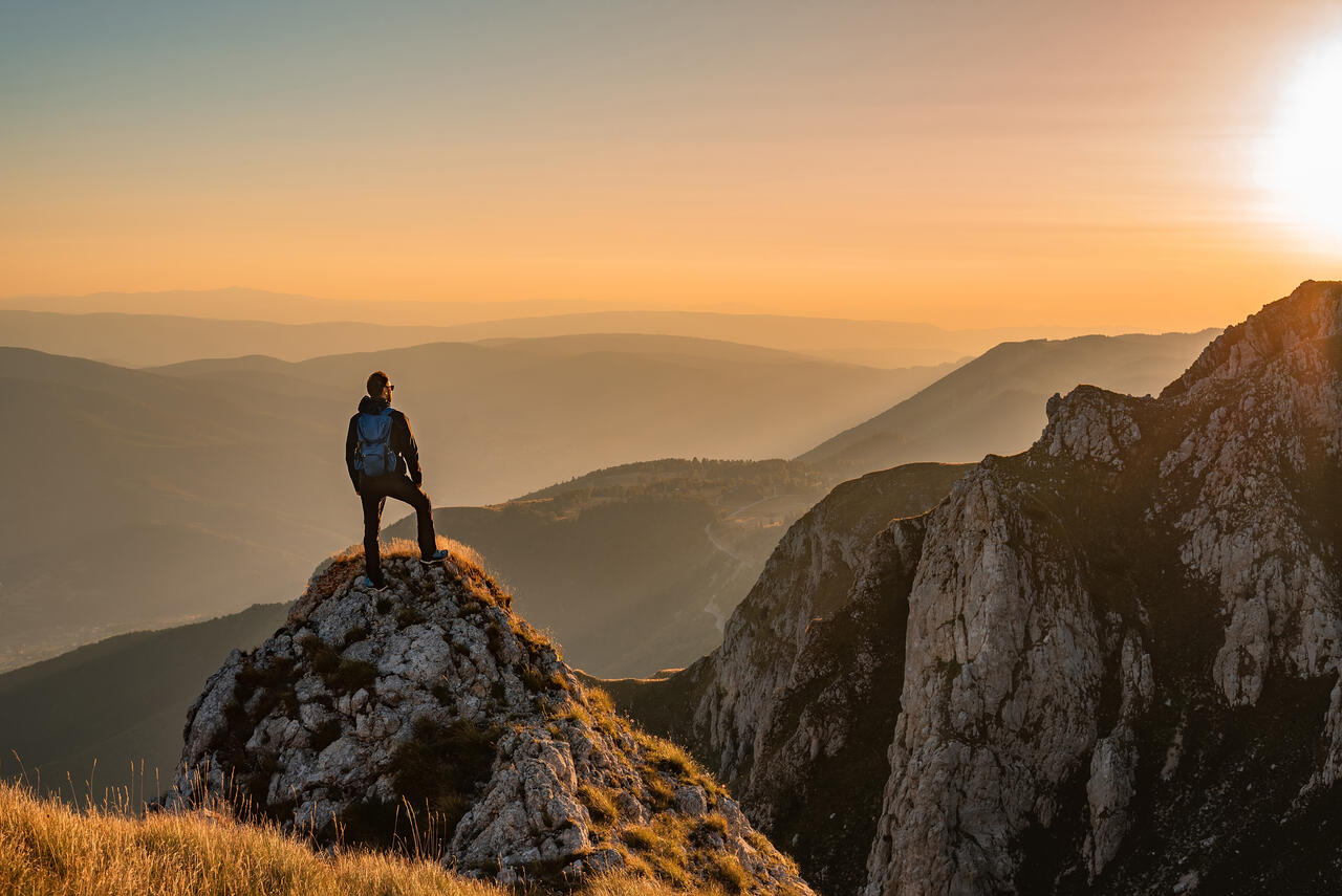 A man stands atop a mountain, gazing at the sunset